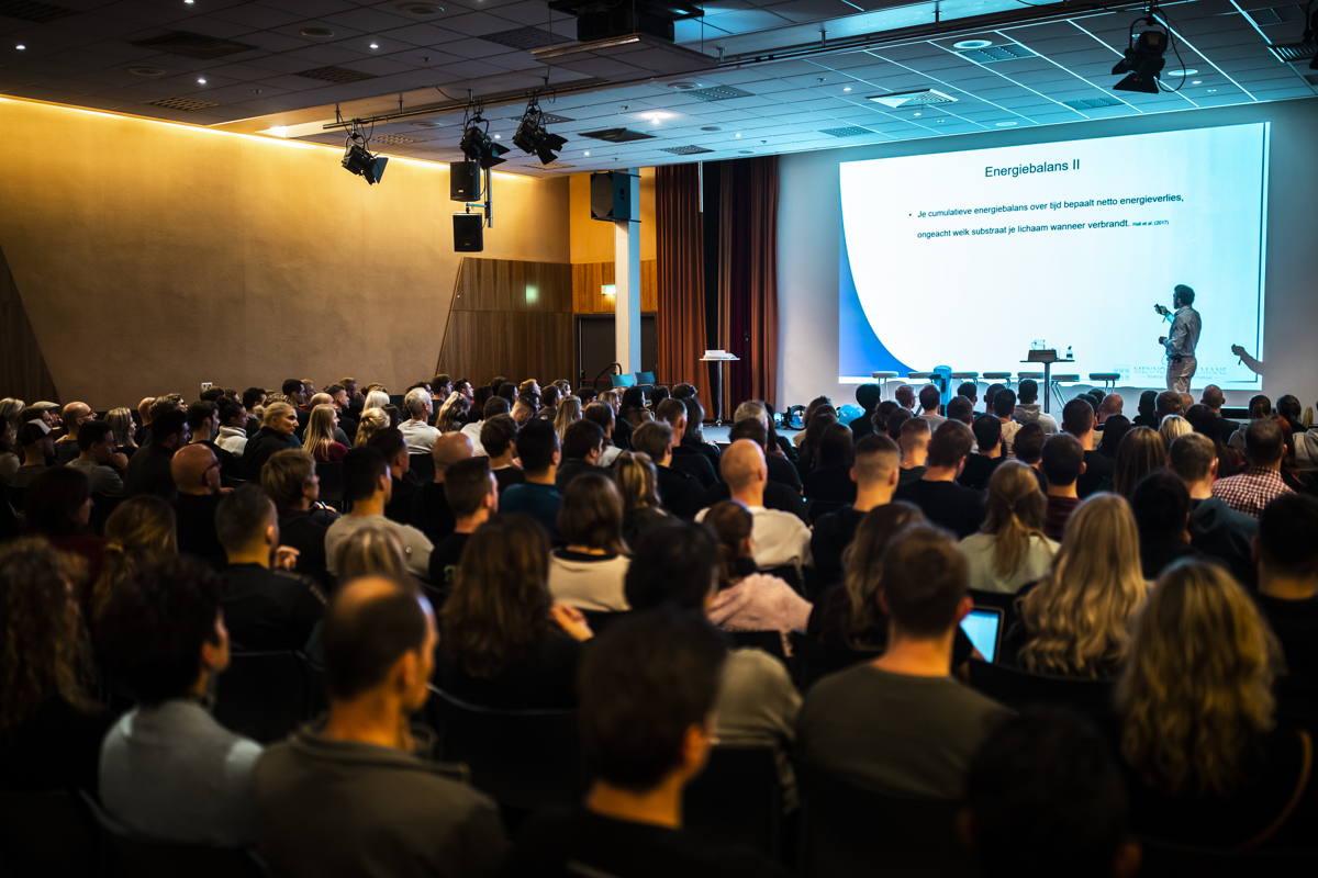 Menno Henselmans presenting to a full auditorium at a live seminar.